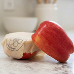 Red apple wrapped with a Beeusable Beeswax Wrap on a marble surface