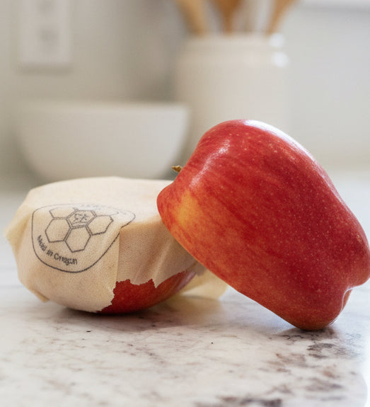 Red apple wrapped with a Beeusable Beeswax Wrap on a marble surface