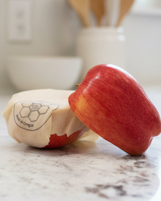 Red apple wrapped with a Beeusable Beeswax Wrap on a marble surface