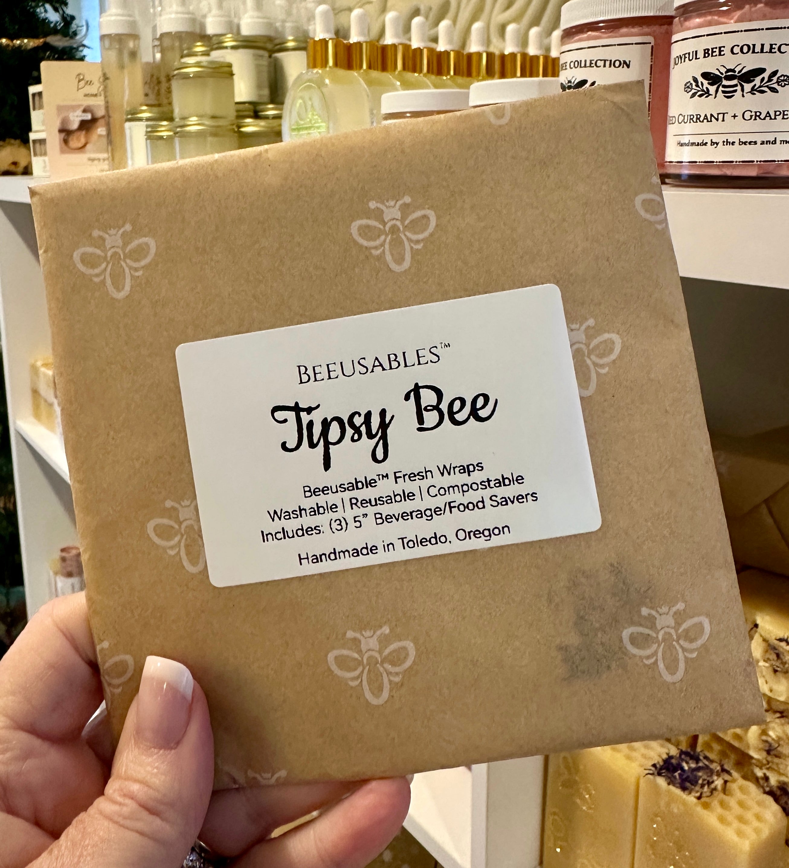 Beeusables Tipsy Bee product packaging held by a hand with a blurred background of similar products.