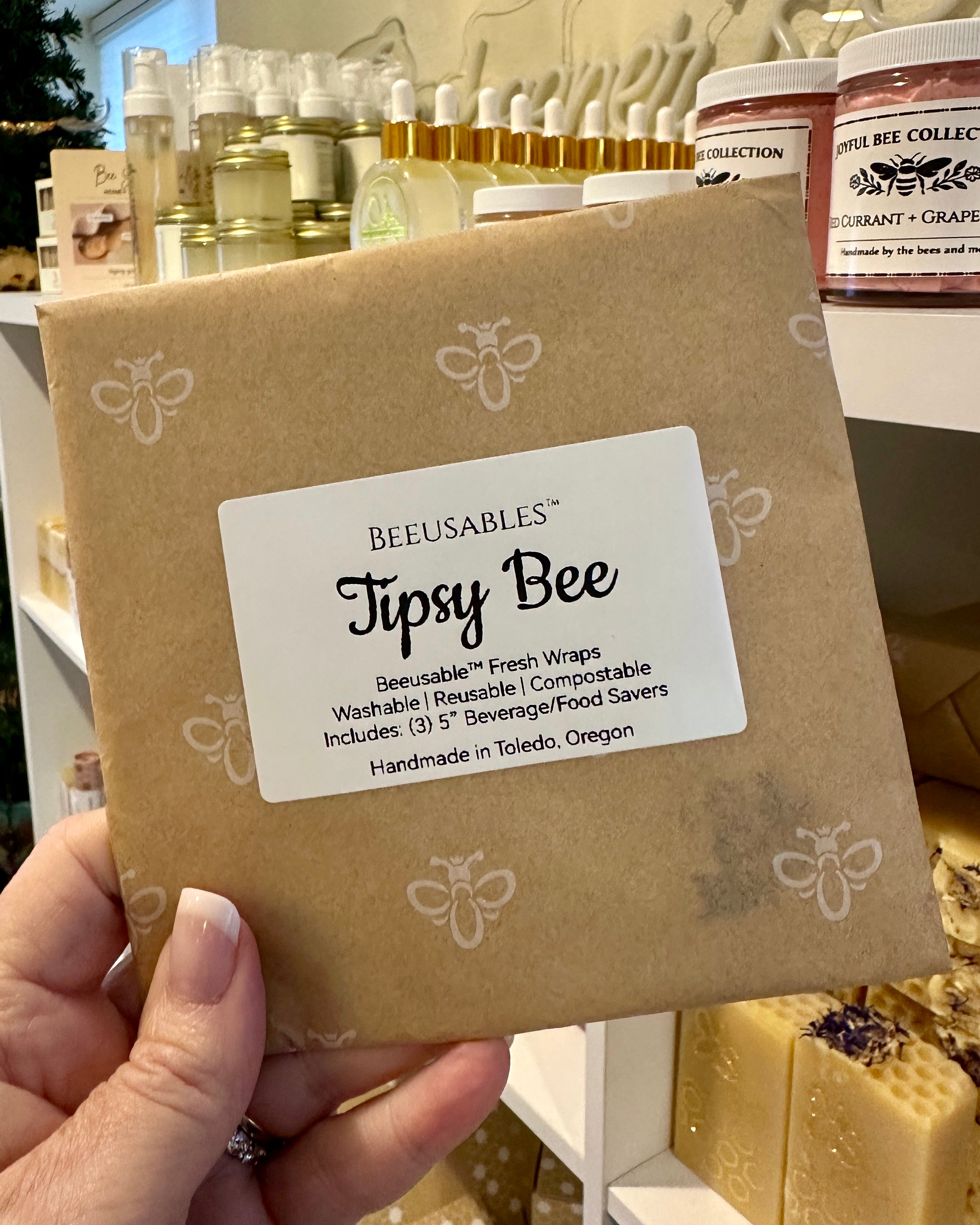 Beeusables Tipsy Bee product packaging held by a hand with a blurred background of similar products.
