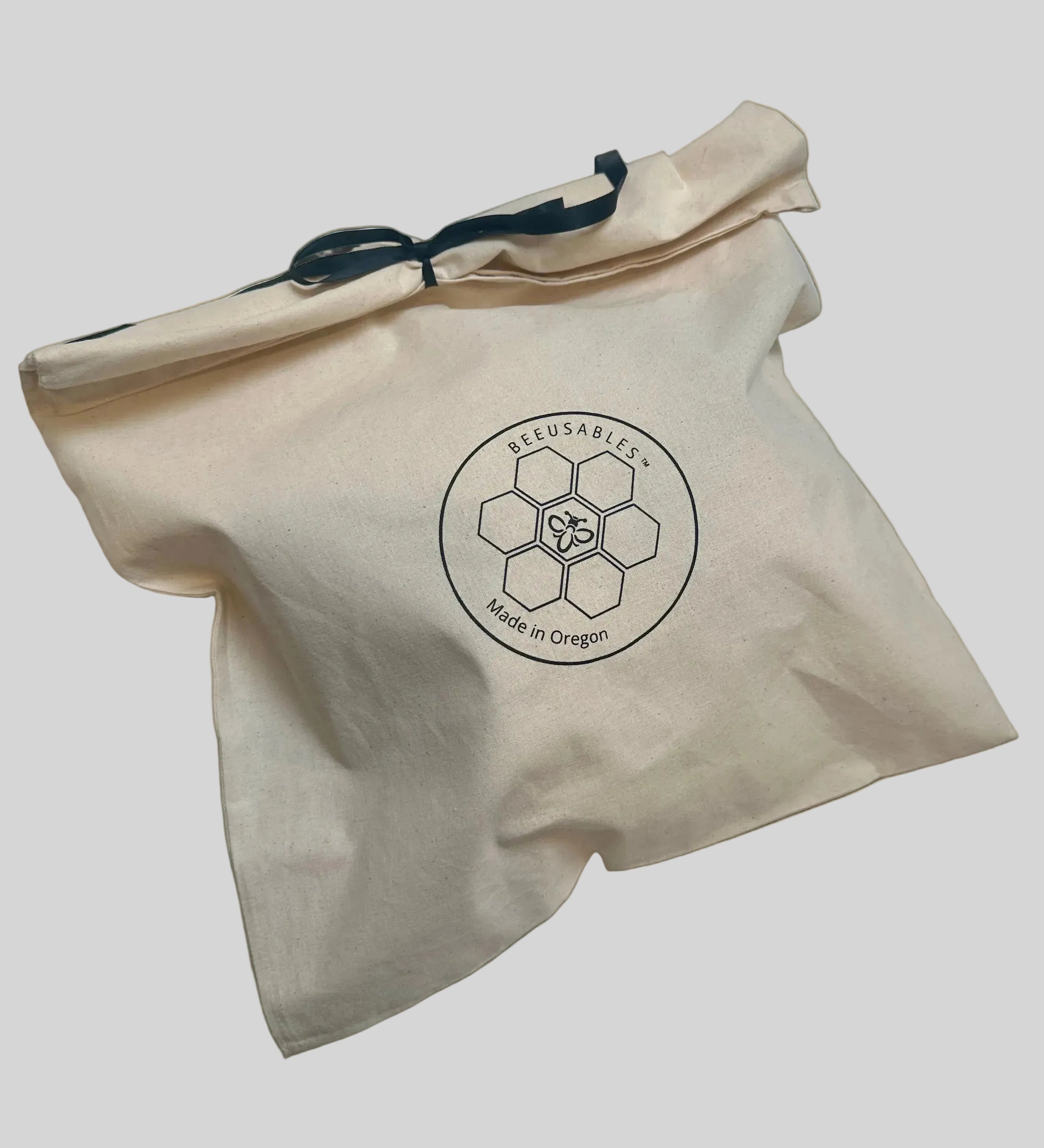 A beige cotton drawstring bag with a black logo printed on the front reading 'BEEUSABLES' and 'Made in Oregon', photographed on a white surface.