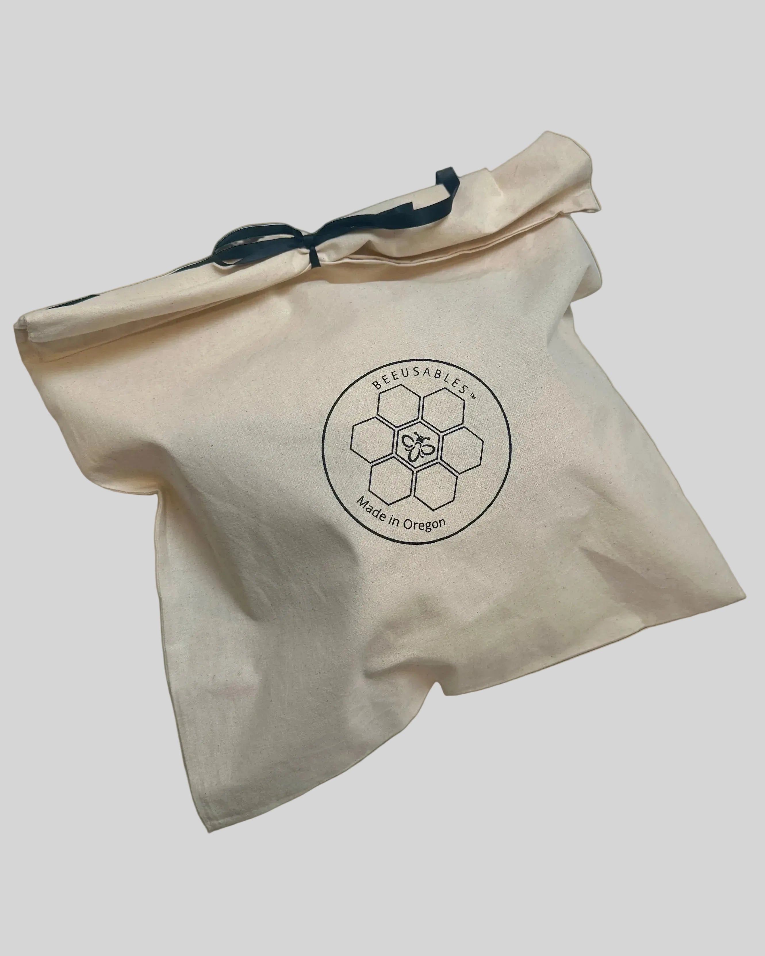 A beige cotton drawstring bag with a black logo printed on the front reading 'BEEUSABLES' and 'Made in Oregon', photographed on a white surface.