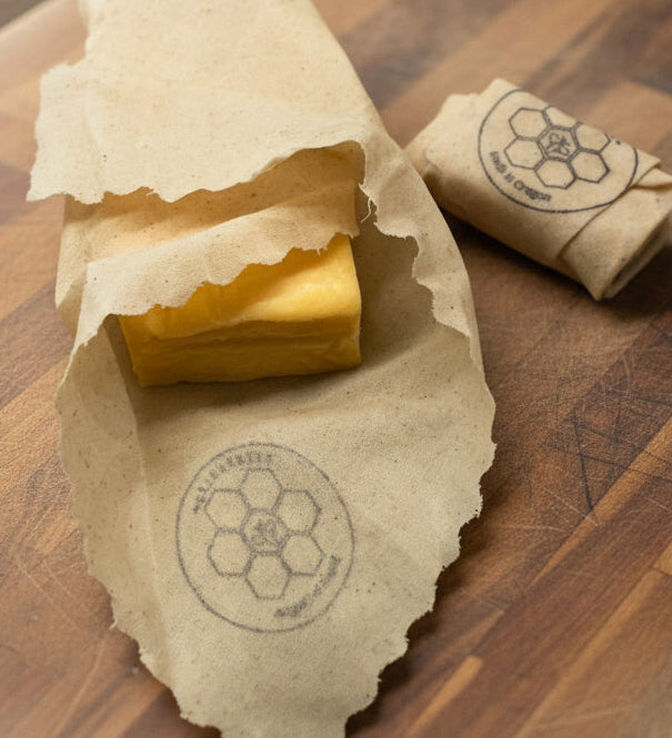 Block of cheese wrapped in a Queen Bee Beeusable Beeswax Wrap on a wooden surface