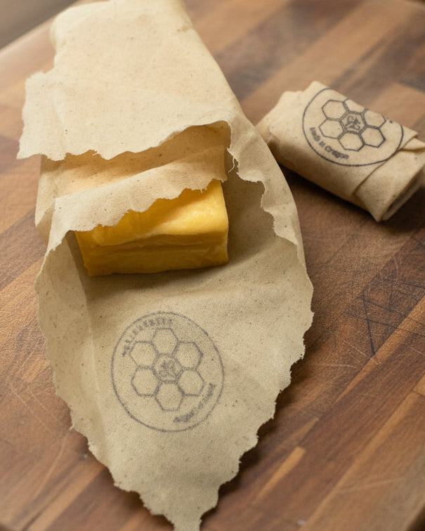 Block of cheese wrapped in a Queen Bee Beeusable Beeswax Wrap on a wooden surface