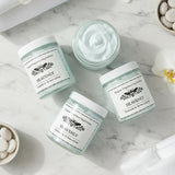 Flat lay of 4 jars of light blue whipped body butter. one open showing the conents.