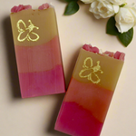 Two layered soap bars with a Bee Logo design on a beige background with white flowers.