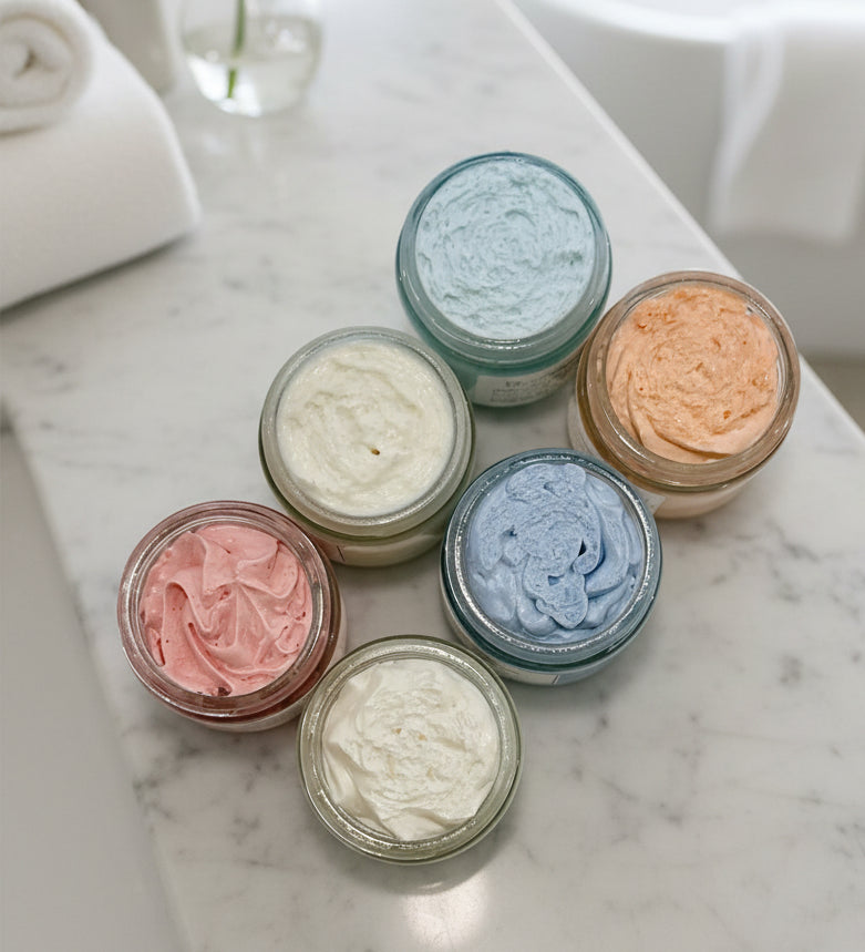 Six small jars with colorful whipped body butter on a white surface