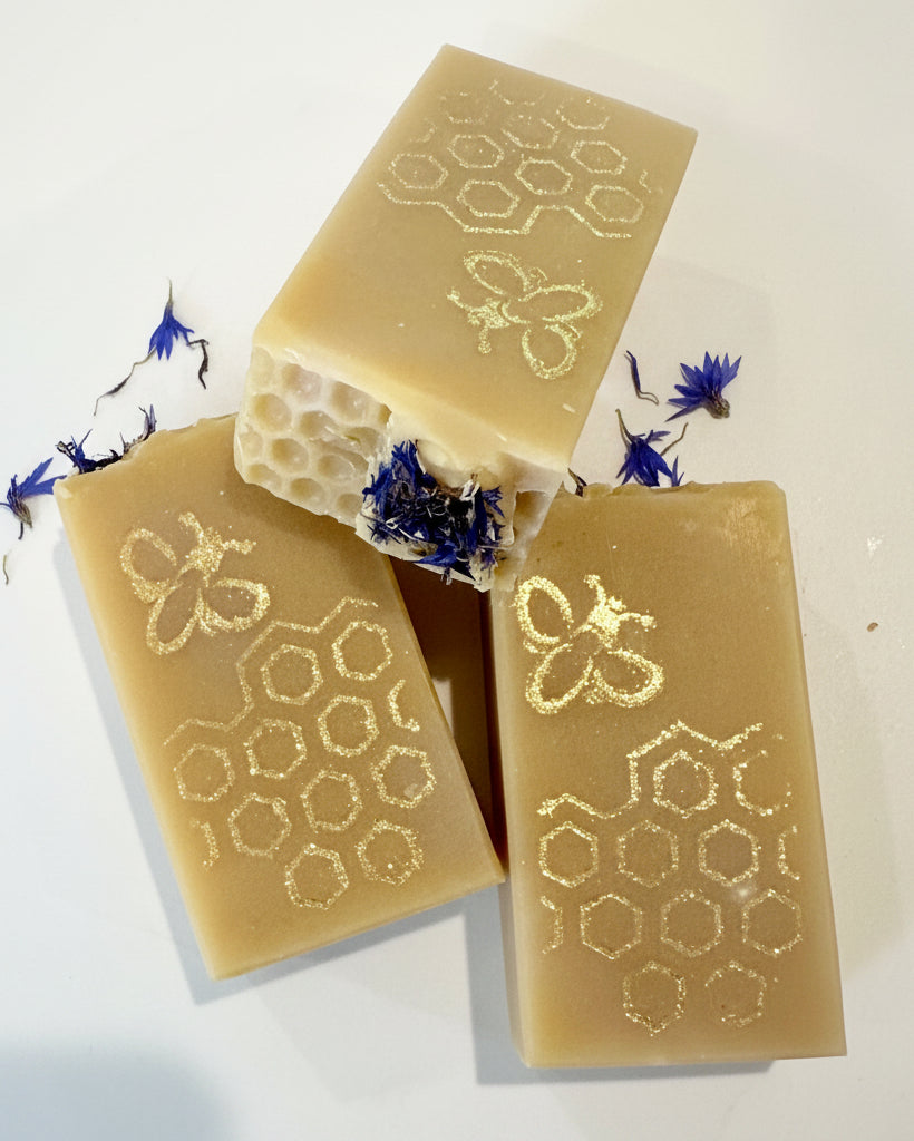 Three bars of soap with honeycomb and bee designs on a white background