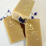 Three bars of soap with honeycomb and bee designs on a white background