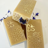 Three bars of soap with honeycomb and bee designs on a white background