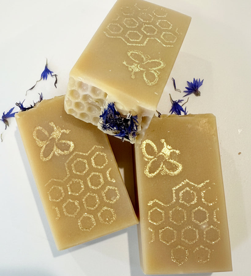 Three bars of soap with honeycomb and bee designs on a white background