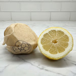 Lemon with half-cut wrapped with a Beeusable Tipsy Bee wrap on a marble surface with tiled wall background