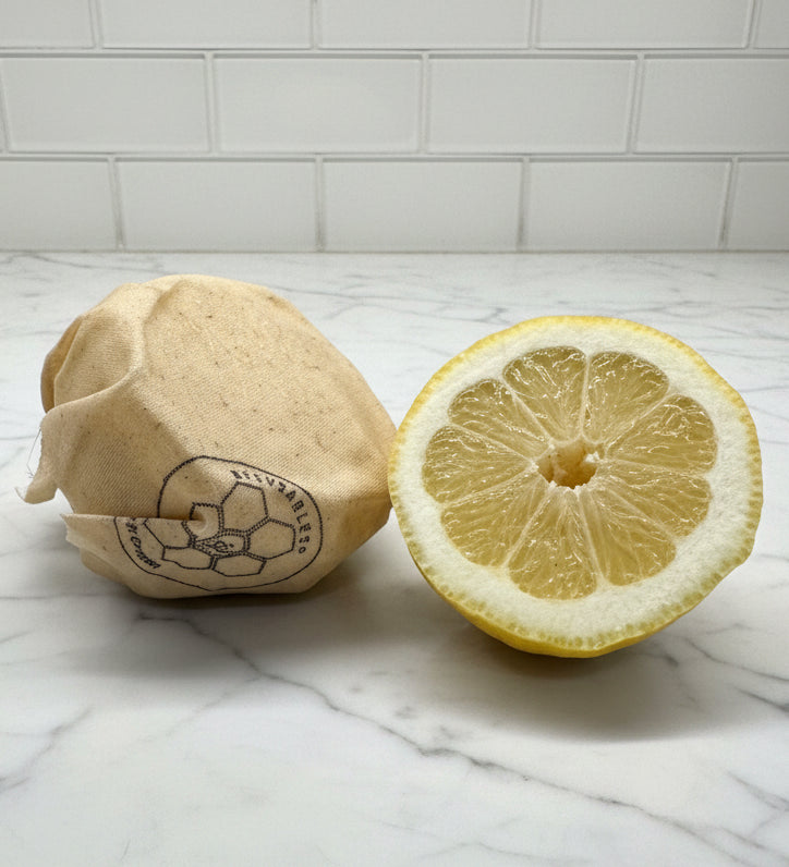 Lemon with half-cut wrapped with a Beeusable Tipsy Bee wrap on a marble surface with tiled wall background