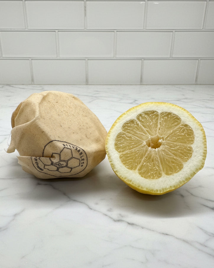 Lemon with half-cut wrapped with a Beeusable Tipsy Bee wrap on a marble surface with tiled wall background