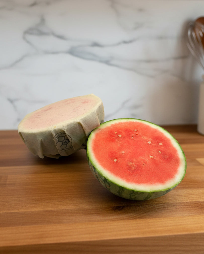 Half cut watermelon on a counter with a beeusable beeswax wrap covering one.