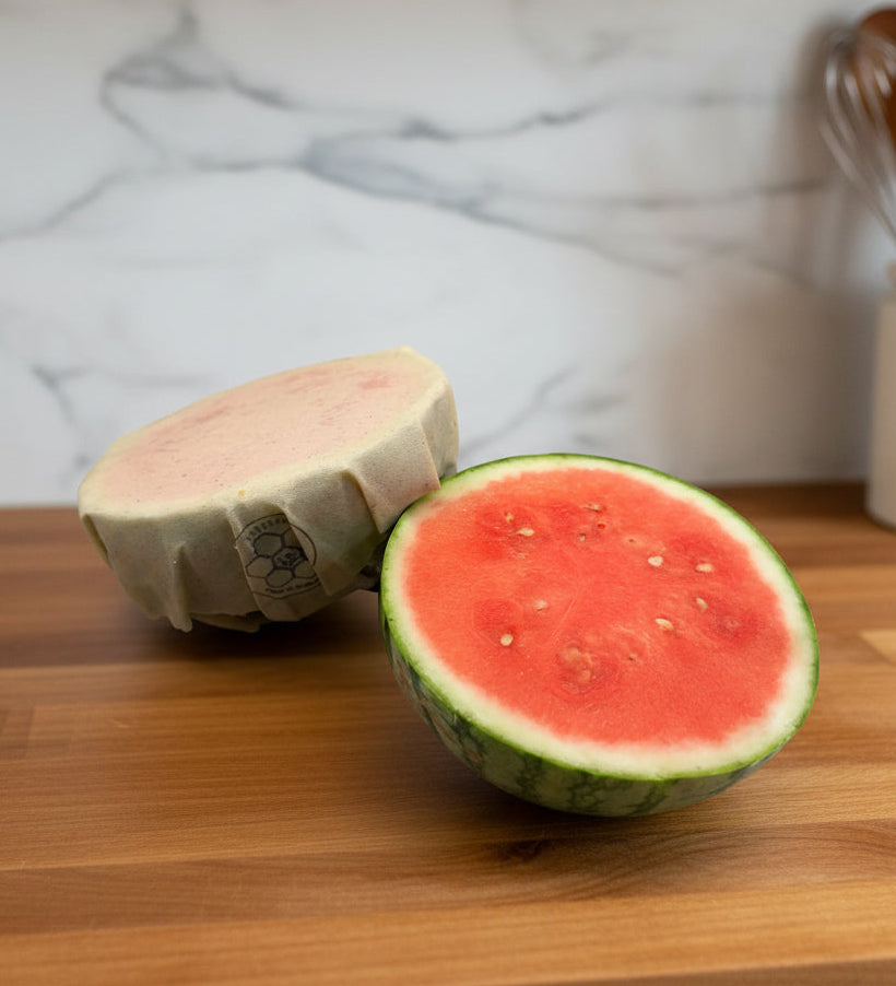 Half cut watermelon on a counter with a beeusable beeswax wrap covering one.